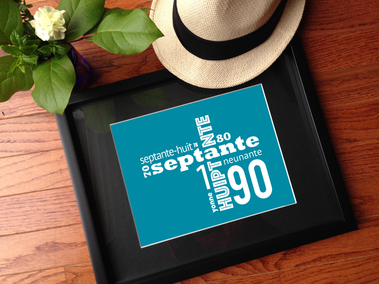 A Acadian numbers print, framed with a hat and greenery near it.
