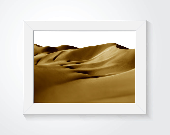 Framed photo of sand dunes hung on a white wall.