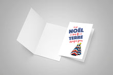 One open blank greeting card. A second greeting card closed with the front visible with an Acadian Christmas song lyrics.