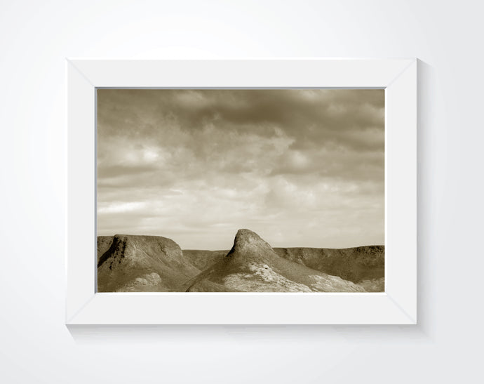 A photograph of a desert in sepia tones framed and on a white wall.